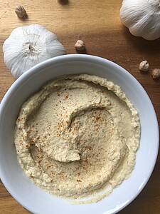 Eine Schale mit Hummus, daneben Knoblauch und Kichererbsen